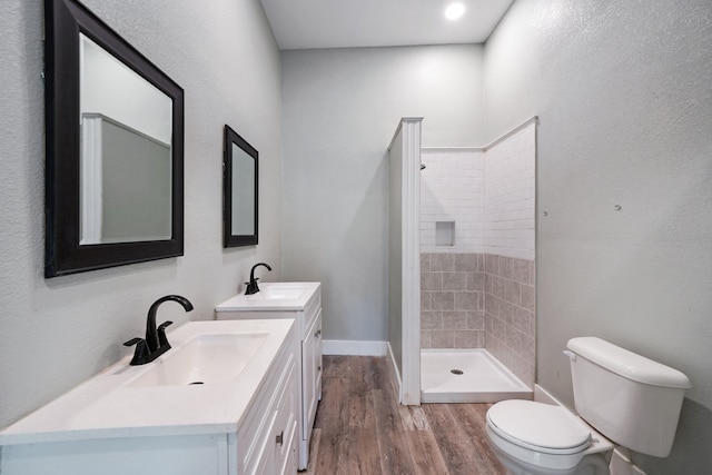 bathroom featuring hardwood / wood-style flooring, vanity, tiled shower, and toilet