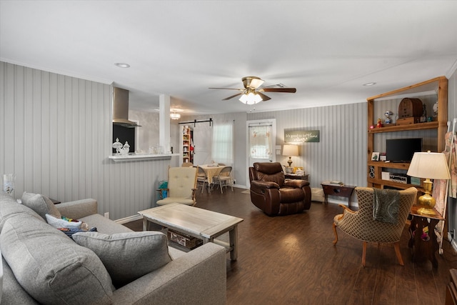 living room featuring a barn door, ornamental molding, dark hardwood / wood-style floors, and ceiling fan