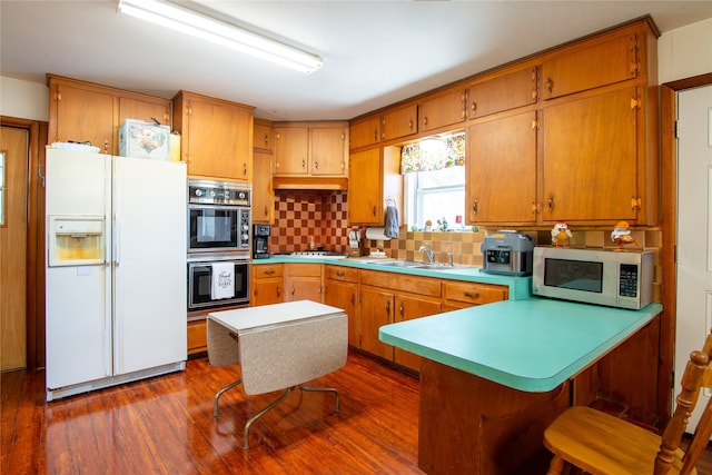 kitchen featuring dark wood-type flooring, kitchen peninsula, stainless steel appliances, sink, and tasteful backsplash