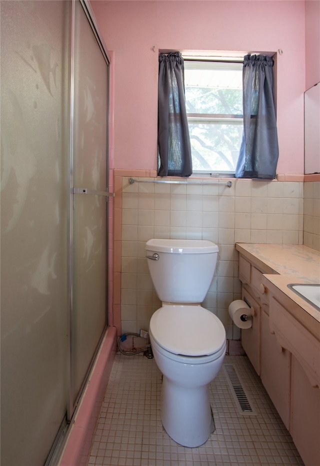 bathroom with tile walls, toilet, vanity, an enclosed shower, and tile patterned floors