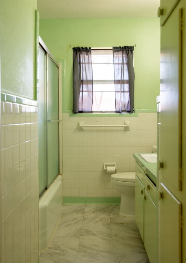 full bathroom with tile walls, vanity, shower / bath combination with glass door, and toilet