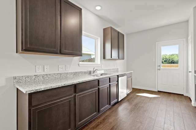 kitchen featuring dark hardwood / wood-style flooring, light stone countertops, stainless steel dishwasher, dark brown cabinetry, and sink