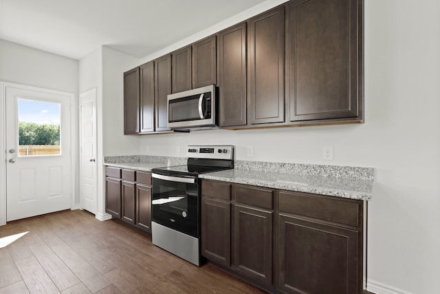 kitchen with dark wood-type flooring, dark brown cabinets, appliances with stainless steel finishes, and light stone counters