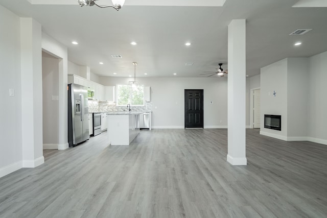 kitchen featuring white cabinets, light wood-type flooring, appliances with stainless steel finishes, decorative light fixtures, and a kitchen island