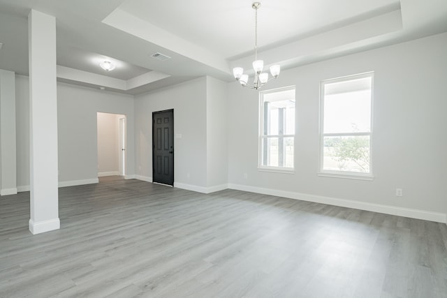 unfurnished room with a tray ceiling, light hardwood / wood-style flooring, and a notable chandelier