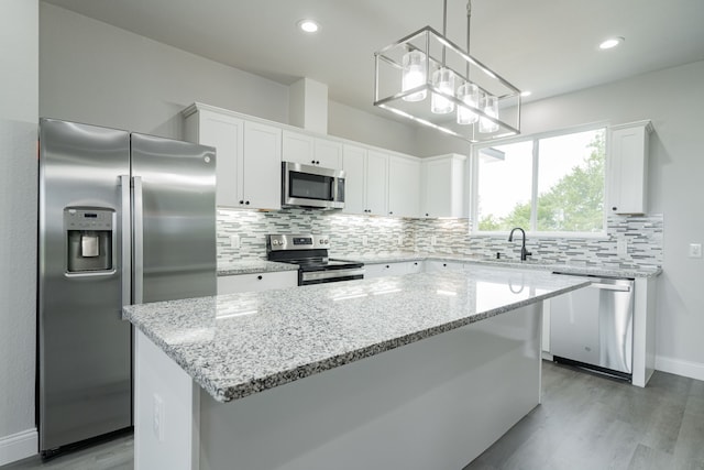 kitchen with a center island, white cabinets, stainless steel appliances, and decorative light fixtures