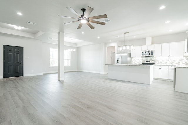 unfurnished living room featuring a raised ceiling, light hardwood / wood-style floors, and ceiling fan with notable chandelier