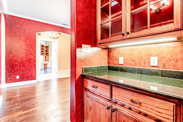 kitchen featuring light wood-type flooring, an inviting chandelier, ornamental molding, and dark stone countertops