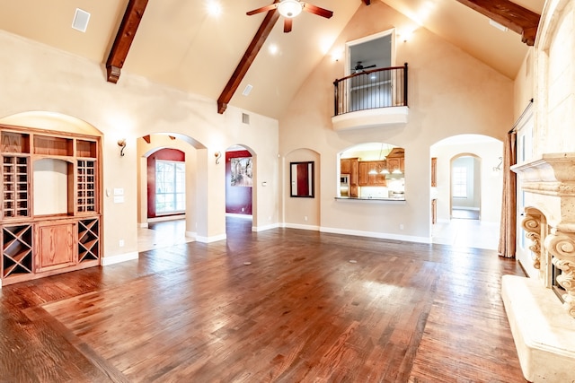 living area with beam ceiling, wood finished floors, arched walkways, and ceiling fan