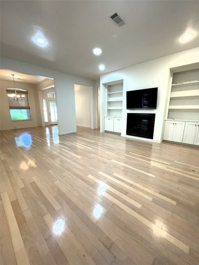 unfurnished living room featuring an inviting chandelier, built in shelves, a textured ceiling, and light wood-type flooring