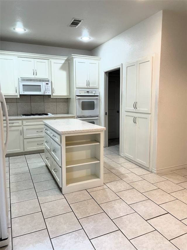 kitchen with white cabinets, a kitchen island, decorative backsplash, white appliances, and light tile patterned floors