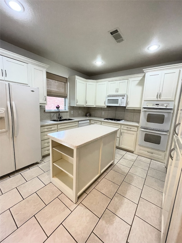 kitchen with white cabinets, white appliances, a kitchen island, and backsplash