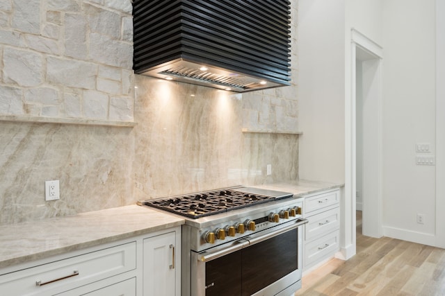 kitchen with tasteful backsplash, high end stainless steel range oven, white cabinetry, light wood-type flooring, and custom range hood