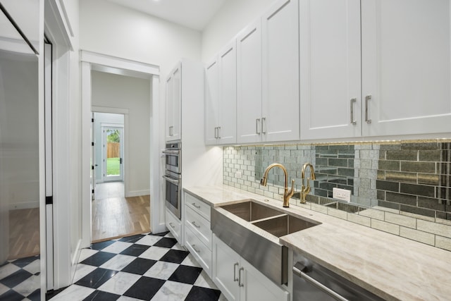 kitchen with light stone countertops, sink, white cabinets, and double oven