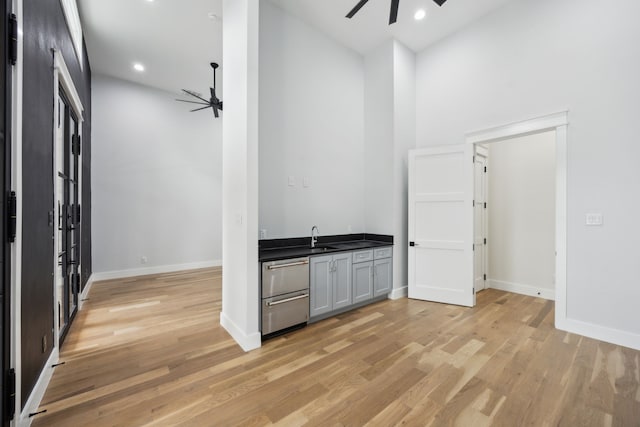 bar with a towering ceiling, sink, light hardwood / wood-style floors, and ceiling fan