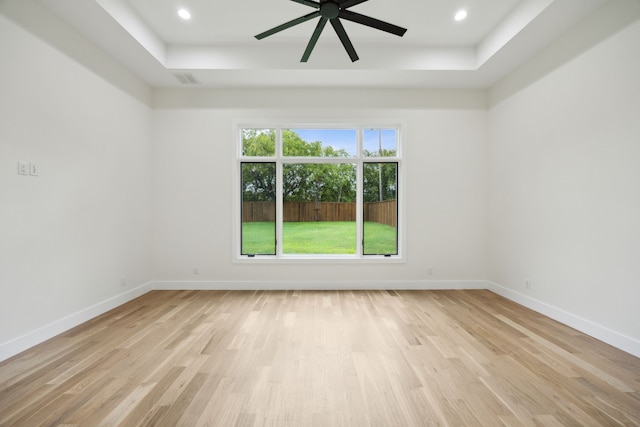 unfurnished room with light hardwood / wood-style floors, a raised ceiling, and ceiling fan