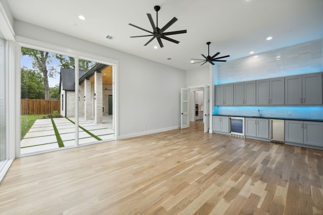 unfurnished living room featuring wine cooler, light hardwood / wood-style floors, and ceiling fan