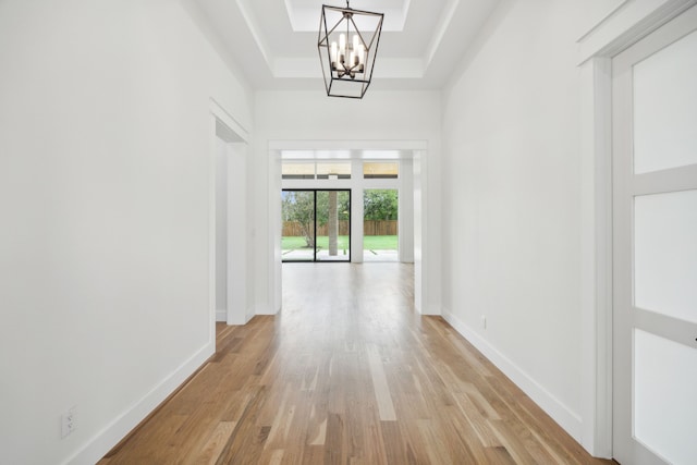 corridor with a chandelier, a tray ceiling, and light hardwood / wood-style floors