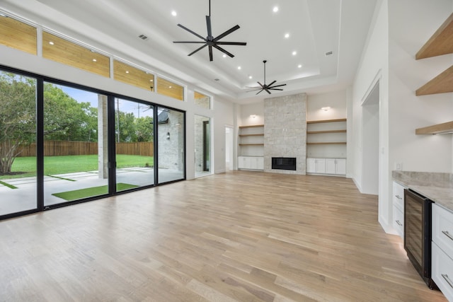 unfurnished living room with wine cooler, light hardwood / wood-style flooring, a fireplace, and ceiling fan