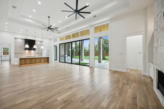 unfurnished living room featuring light hardwood / wood-style floors, a towering ceiling, a tray ceiling, and a fireplace