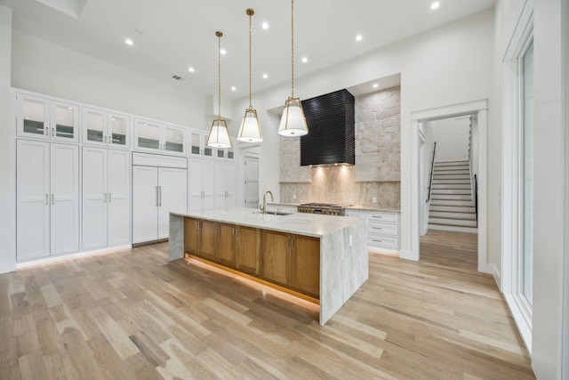 kitchen with sink, hanging light fixtures, a large island, light hardwood / wood-style floors, and white cabinets