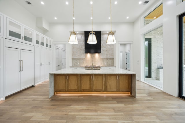 kitchen featuring white cabinetry, light stone counters, light wood-type flooring, and a large island with sink