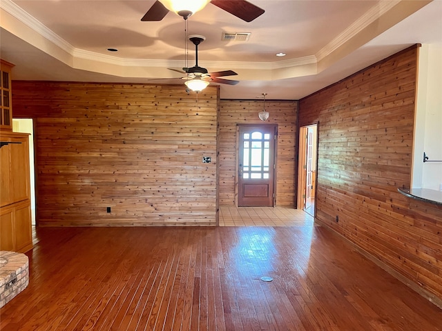 unfurnished room featuring wood-type flooring, a raised ceiling, wooden walls, and ceiling fan