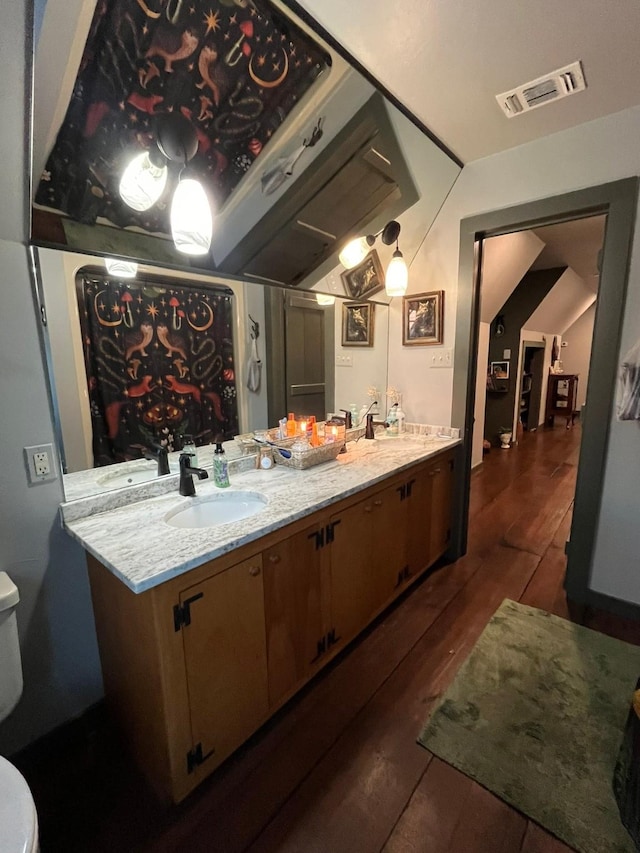 bathroom with hardwood / wood-style flooring, vaulted ceiling, vanity, and toilet