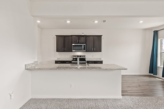 kitchen featuring sink, light hardwood / wood-style flooring, light stone countertops, appliances with stainless steel finishes, and kitchen peninsula