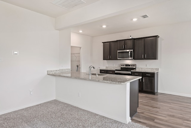 kitchen with light stone countertops, sink, stainless steel appliances, light hardwood / wood-style flooring, and kitchen peninsula