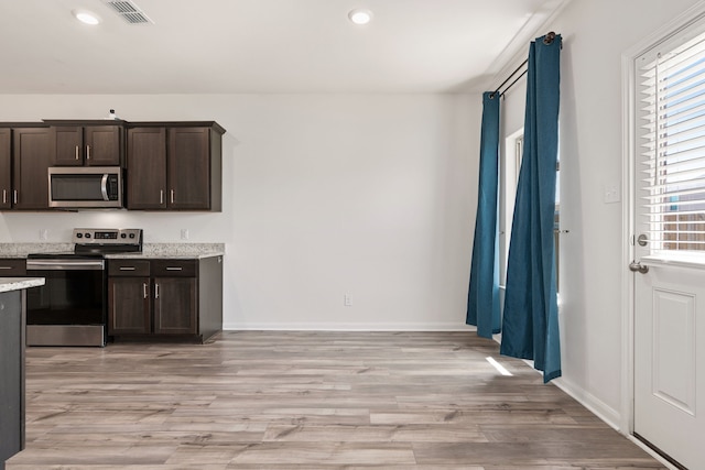 kitchen with dark brown cabinetry, light stone counters, light hardwood / wood-style floors, and appliances with stainless steel finishes