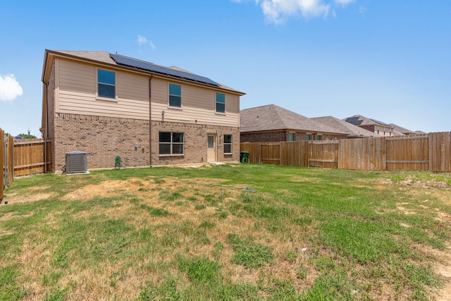 rear view of property with central AC, a yard, and solar panels