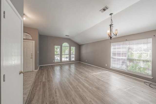 empty room with a chandelier, lofted ceiling, and light hardwood / wood-style floors