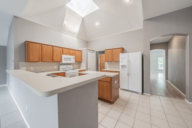 kitchen featuring light hardwood / wood-style flooring, white appliances, kitchen peninsula, a skylight, and high vaulted ceiling