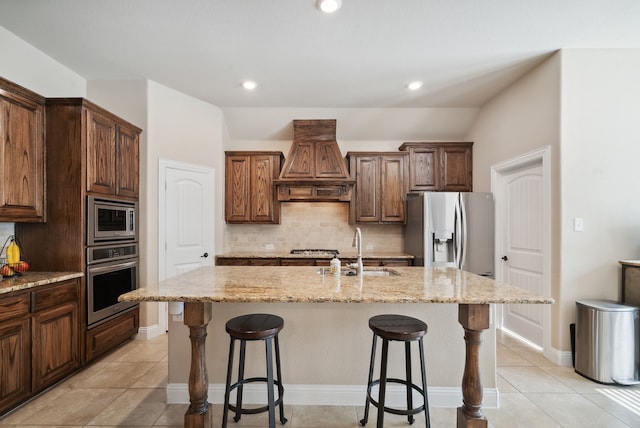 kitchen with tasteful backsplash, custom exhaust hood, appliances with stainless steel finishes, sink, and a center island with sink