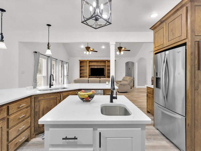 kitchen featuring stainless steel refrigerator with ice dispenser, ceiling fan with notable chandelier, a center island with sink, and light wood-type flooring