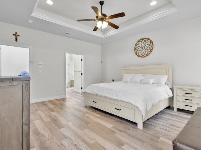 bedroom featuring a raised ceiling, ensuite bath, light wood-type flooring, and ceiling fan