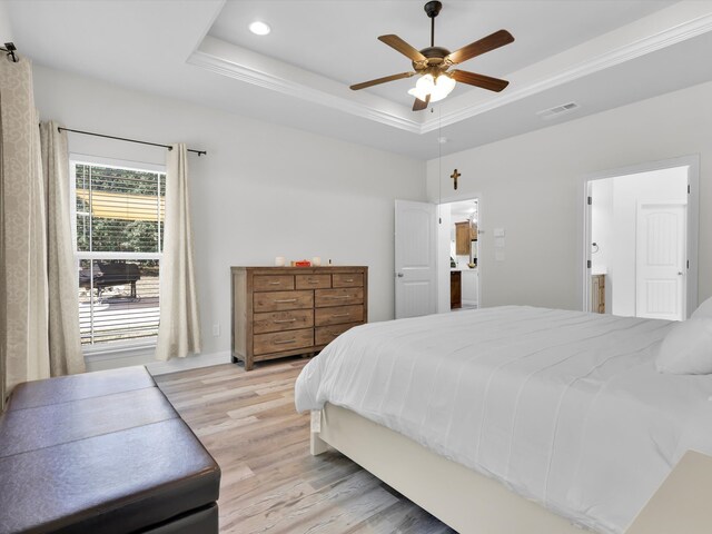 bedroom featuring light hardwood / wood-style flooring, ensuite bath, ceiling fan, and a tray ceiling