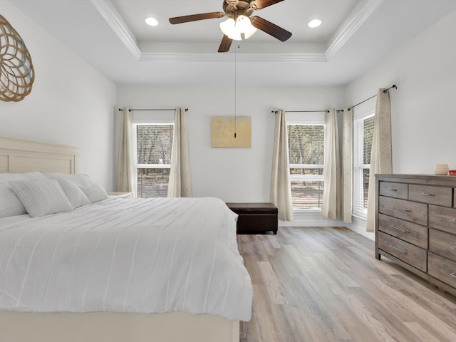 bedroom with light hardwood / wood-style floors, a raised ceiling, multiple windows, and ceiling fan