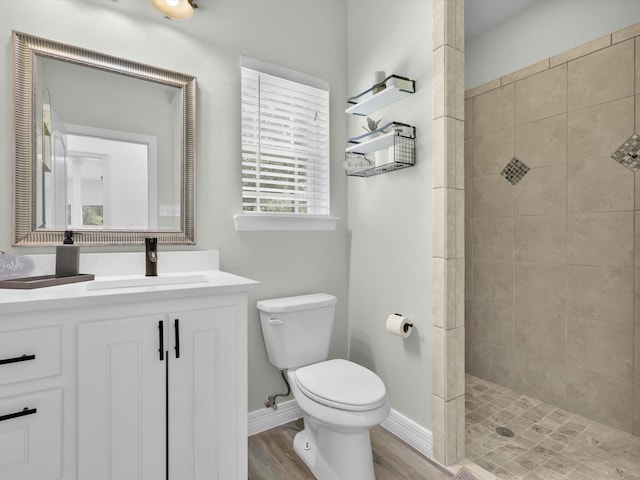 bathroom with vanity, toilet, a tile shower, and wood-type flooring