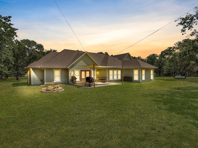 back house at dusk with a patio and a lawn