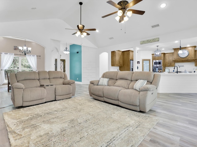 living room featuring ceiling fan with notable chandelier, light hardwood / wood-style flooring, sink, and high vaulted ceiling