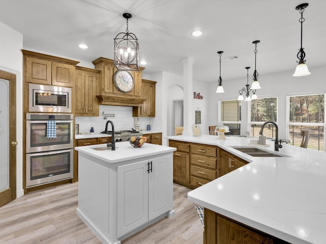 kitchen with appliances with stainless steel finishes, sink, backsplash, a kitchen island with sink, and light wood-type flooring