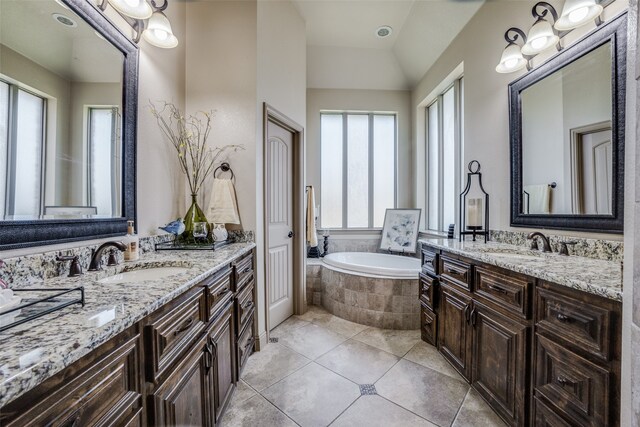 bathroom with tiled bath, tile patterned floors, a wealth of natural light, and double vanity