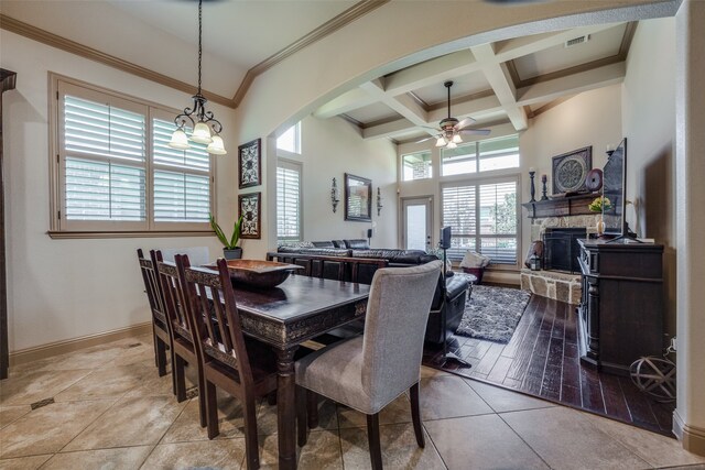 tiled dining room with a stone fireplace, a high ceiling, ceiling fan, ornamental molding, and coffered ceiling