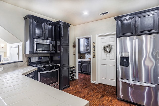 kitchen with stainless steel appliances, dark wood-style flooring, visible vents, tile counters, and tasteful backsplash