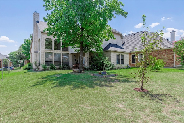 back of property featuring brick siding, a lawn, and a chimney