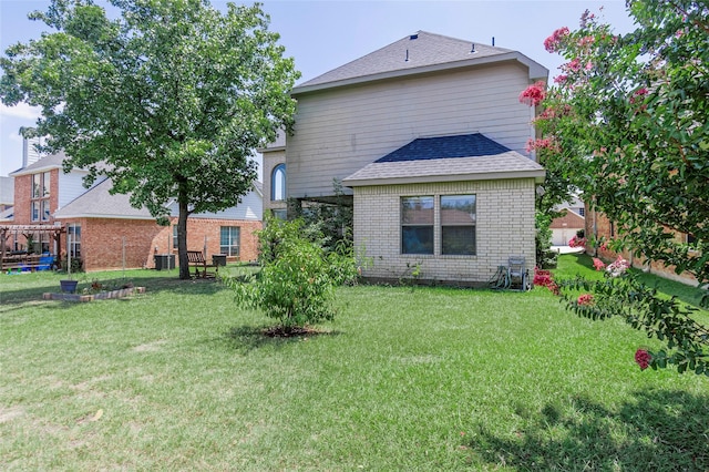 back of property with a yard, roof with shingles, and brick siding