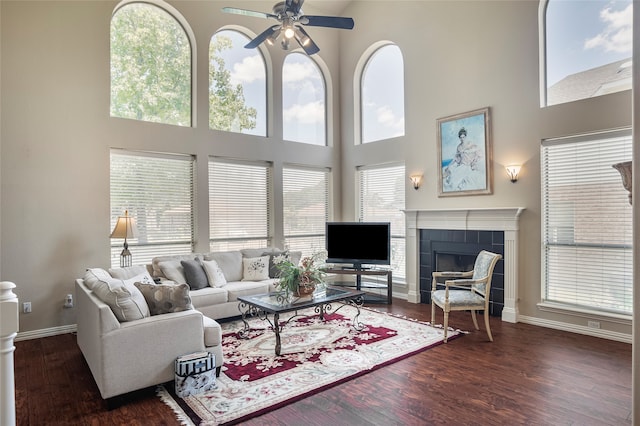 living room featuring dark wood-type flooring, a towering ceiling, a fireplace, and ceiling fan