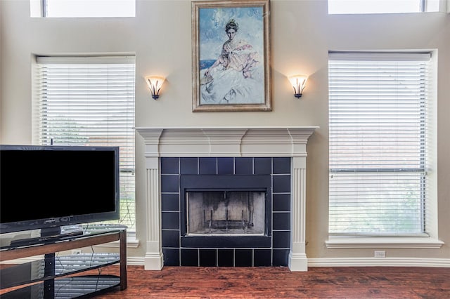 living area featuring a tile fireplace, baseboards, and wood finished floors